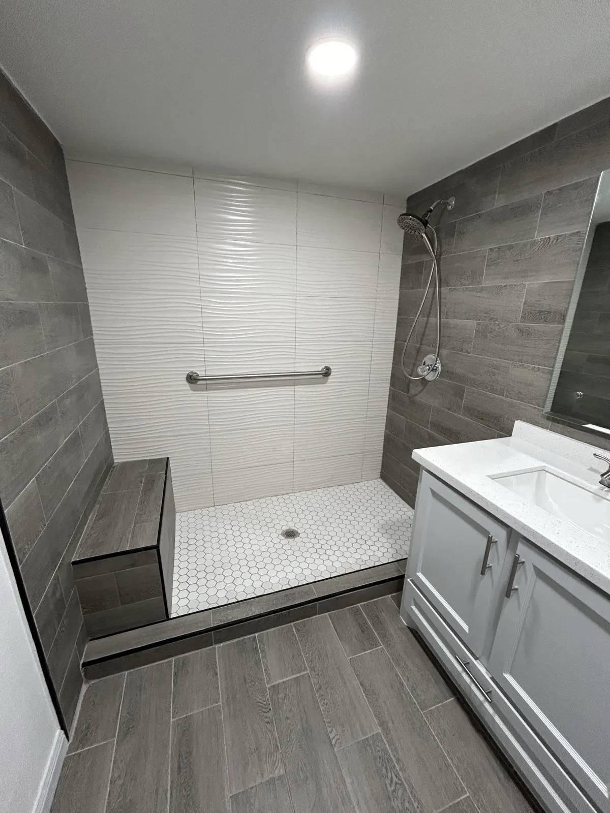 Bathroom after remodel — modern walk-in shower with gray tile and grab bars