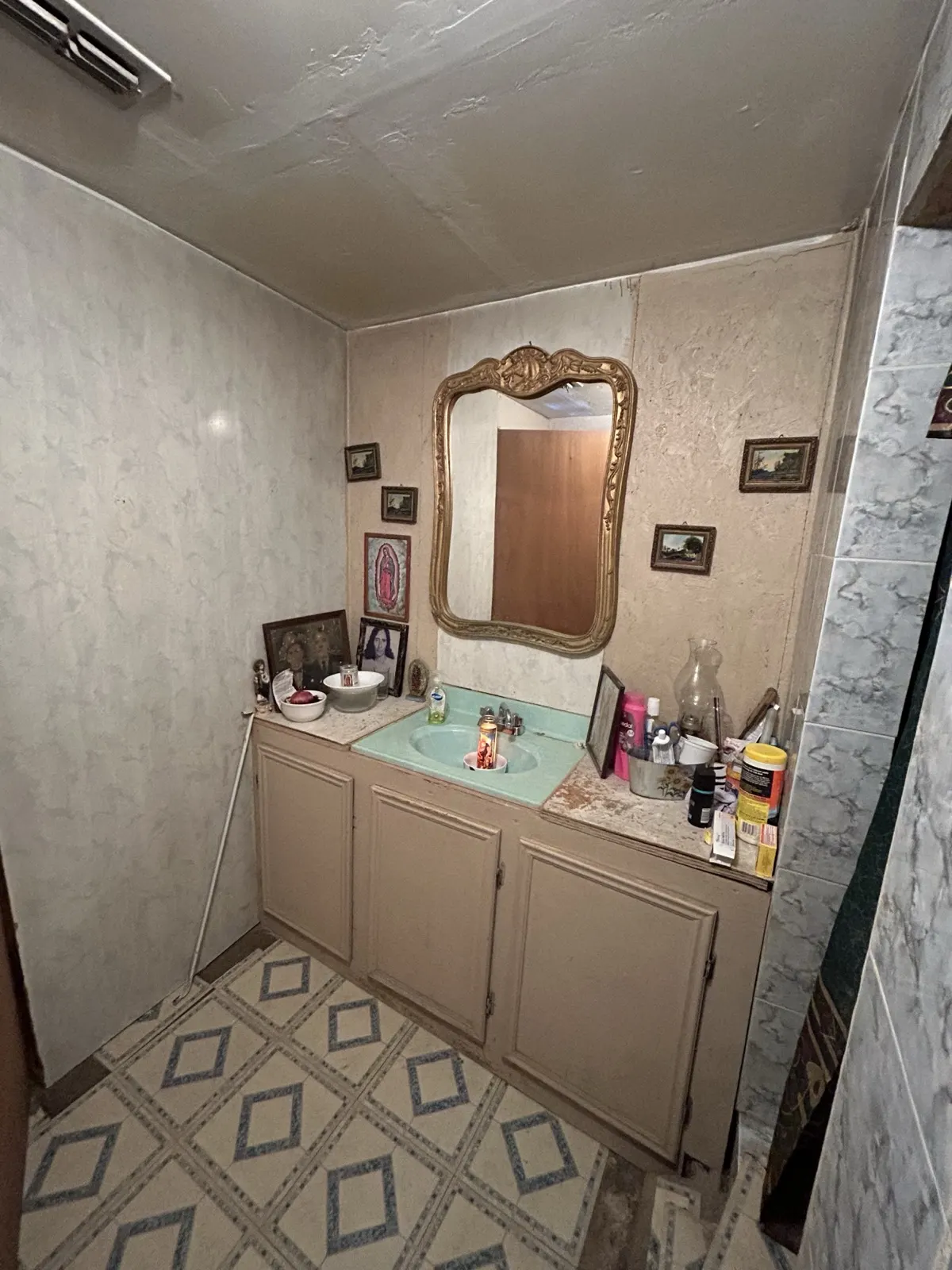 Bathroom before remodel — dated vanity with gold mirror and old flooring