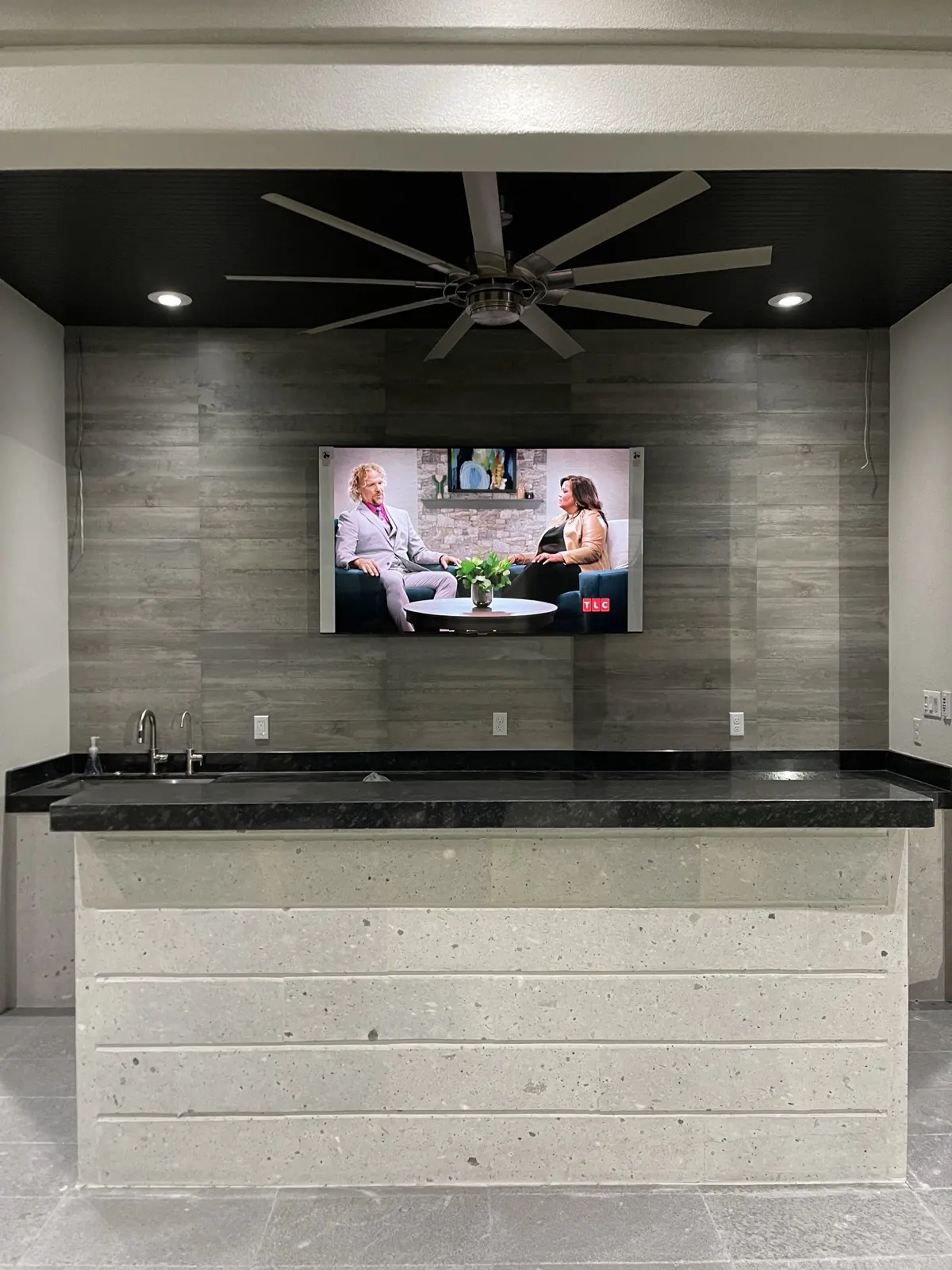 Finished outdoor kitchen interior — TV, ceiling fan, and granite countertop